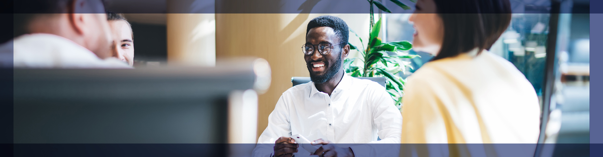 Engaging business meeting with a man smiling joyfully as he discusses ideas with colleagues, set in a vibrant office environment. The image captures a moment of positive interaction, emphasizing teamwork and communication in a professional setting.