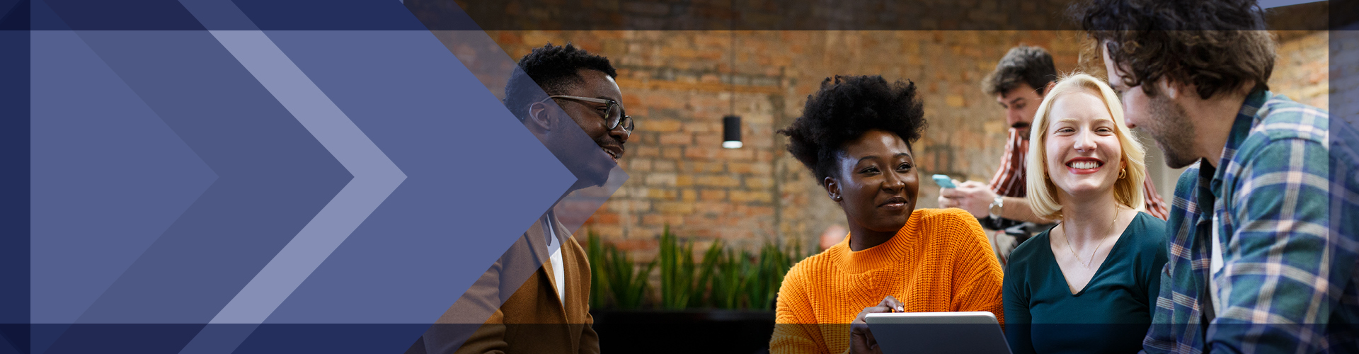 Group of young professionals engaging in a collaborative discussion in a casual office setting with a rustic brick background, showing a diverse team that includes individuals of various ethnicities and backgrounds, all sharing ideas and enjoying a moment of connection